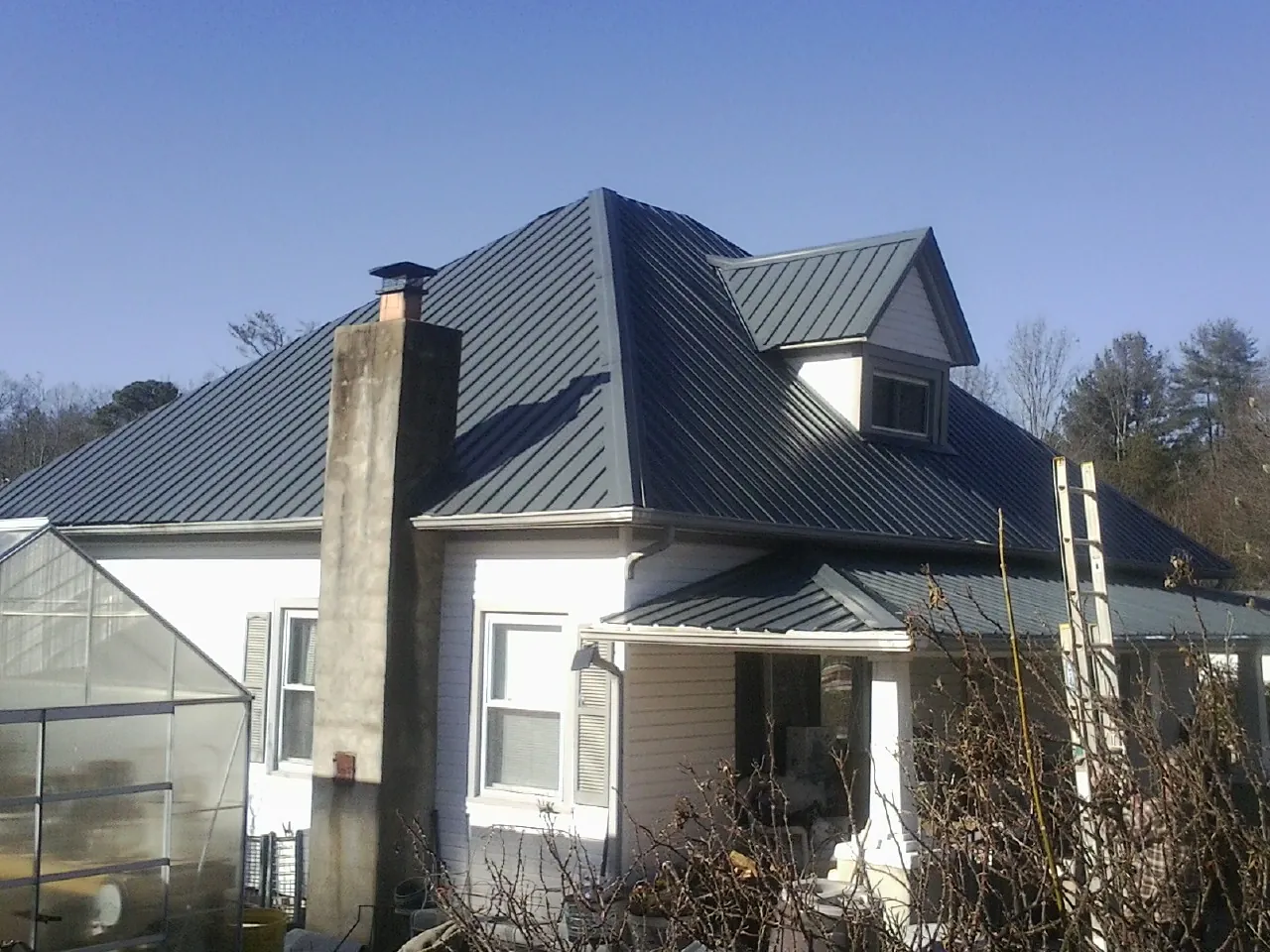 Dark blue standing seam metal roof on a white farmhouse with dormer — Slate & Tile Roof Repair by Roofing Brothers in Shabbona