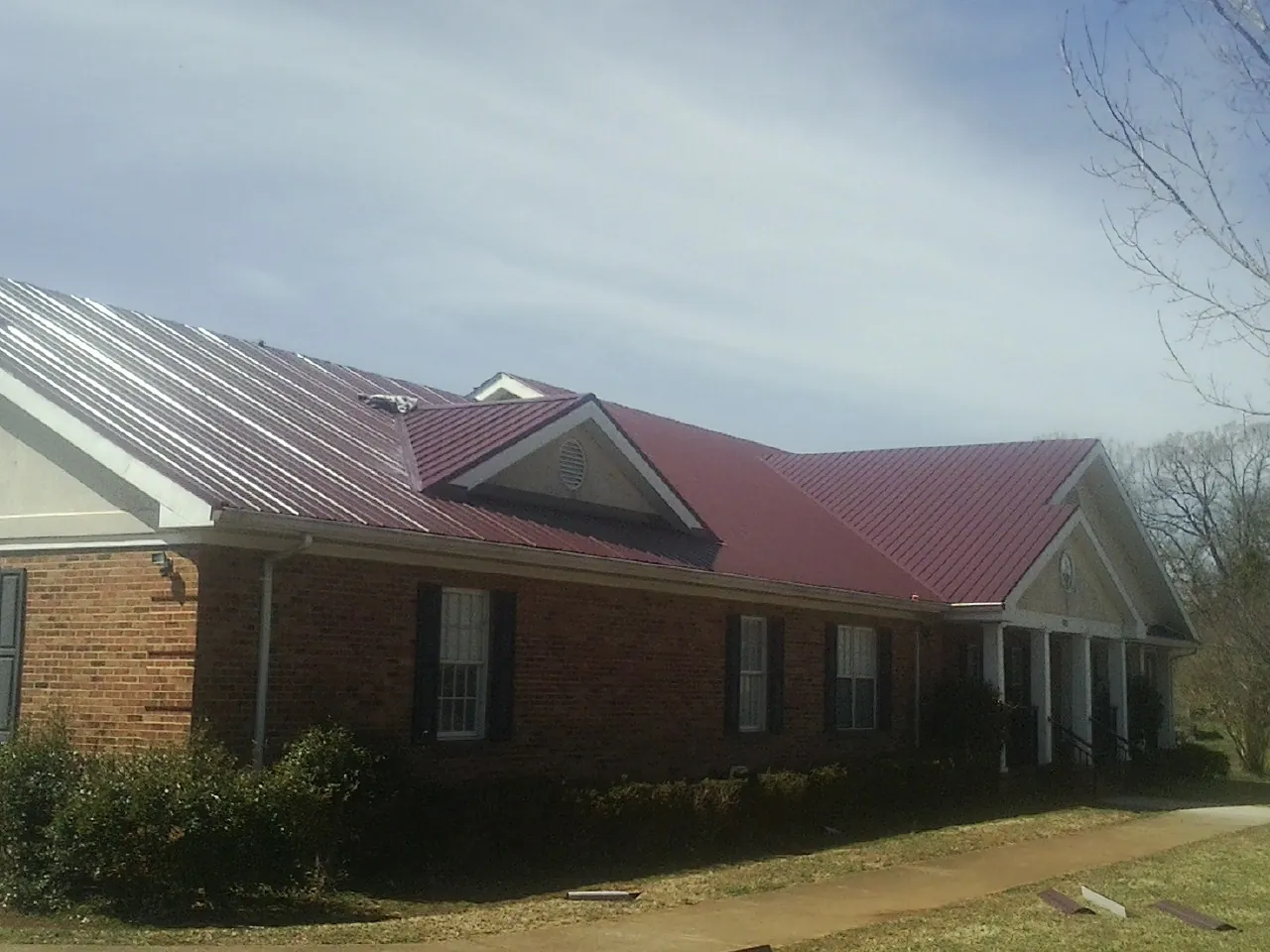 Red metal roof with gabled entries on a long brick building, from a Hail Damage Roof Repair job in Shabbona