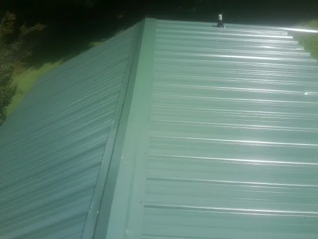 New green metal panels meeting at the ridge of a roof — Flat Roof Repair work by our crew in Shabbona
