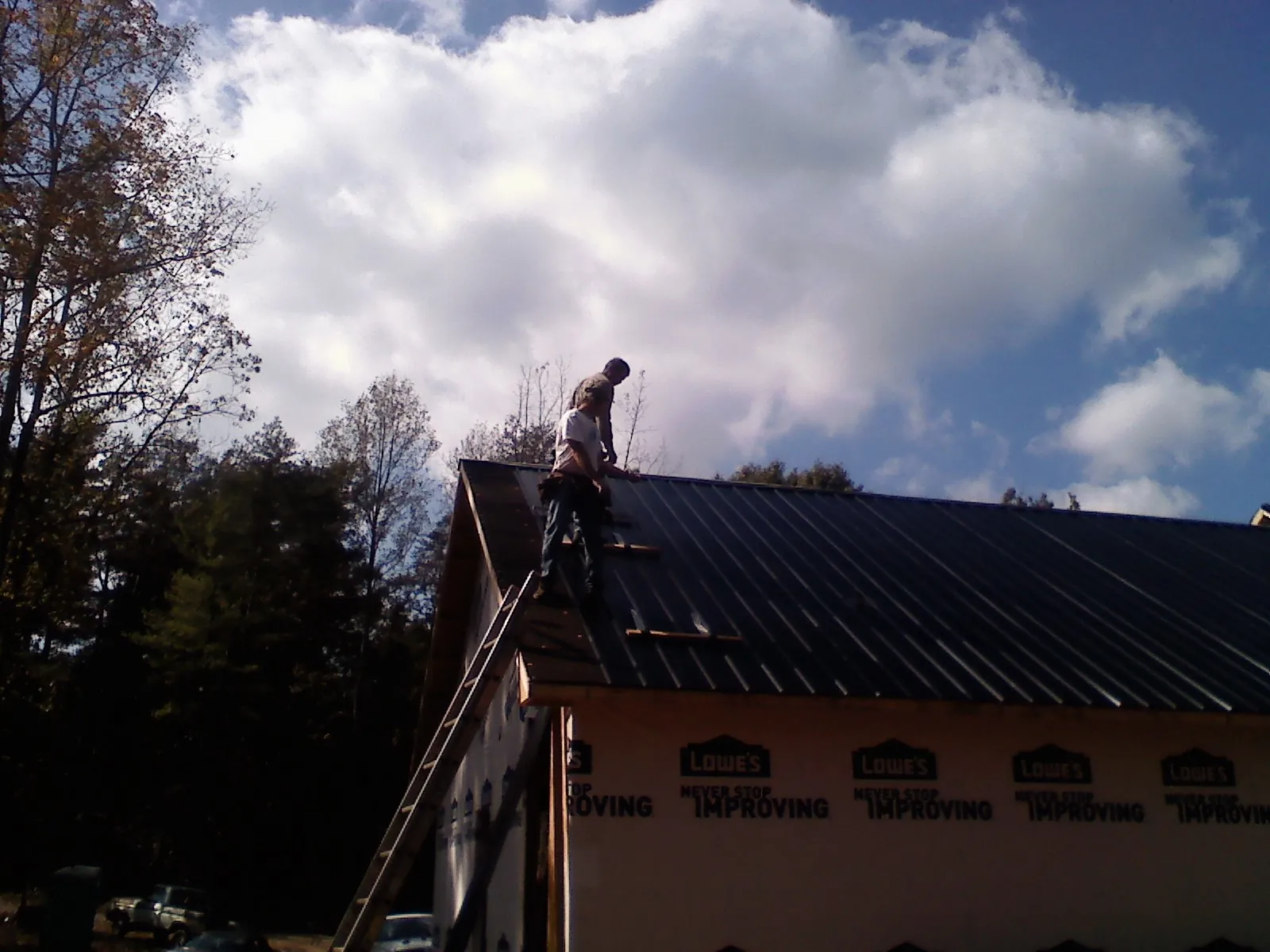 Roofer fastening dark metal panels high against a cloudy sky, from a Roof Inspection job in Shabbona