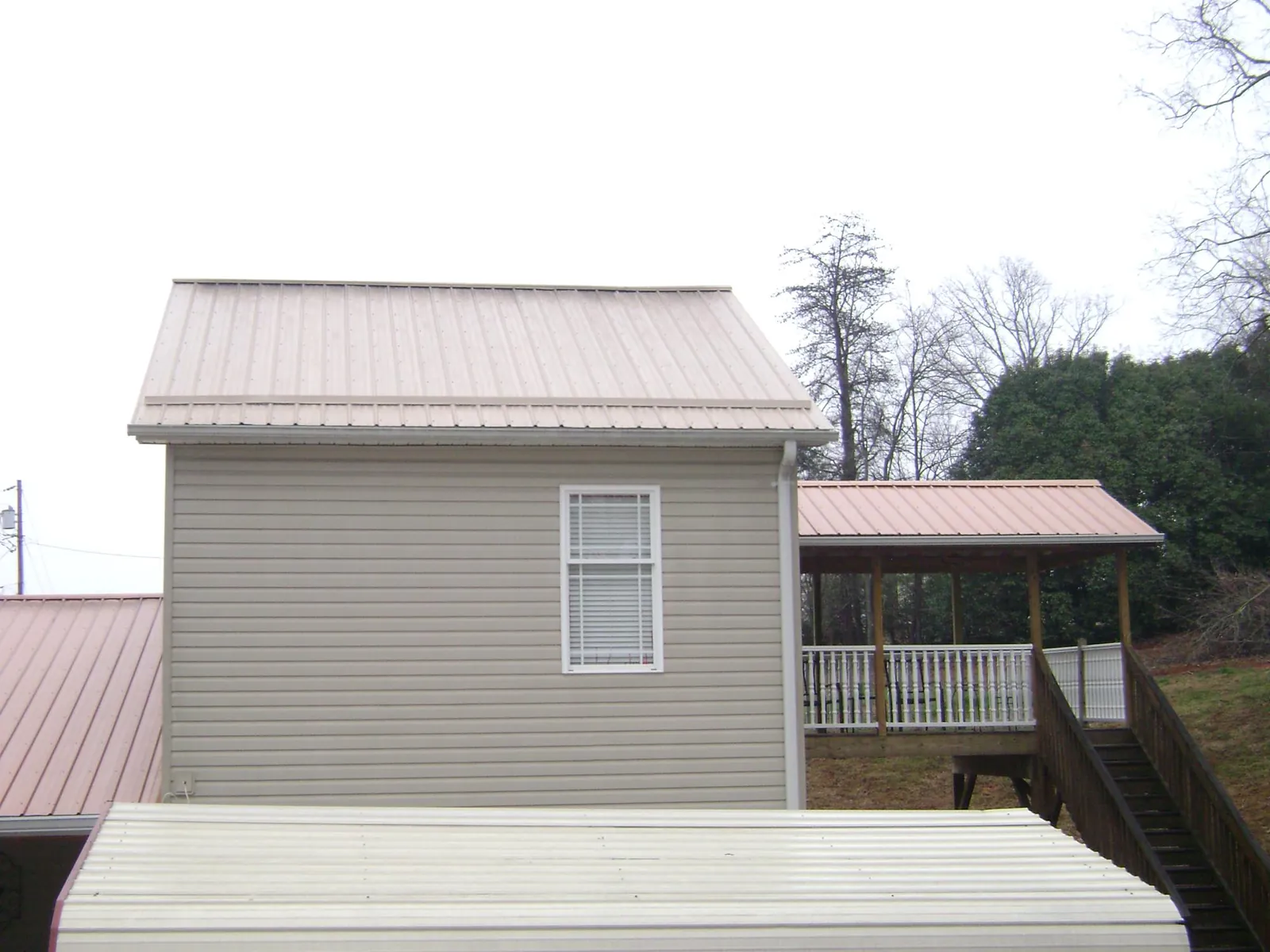 Tan metal roofs on a two story addition and attached porch, from a Roof Replacement job in Shabbona